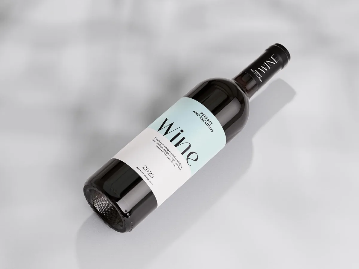Dark wine bottle mockup labelled Wine, Perfect and Exclusive, lying on its side on a light marbled surface with dappled shadow.