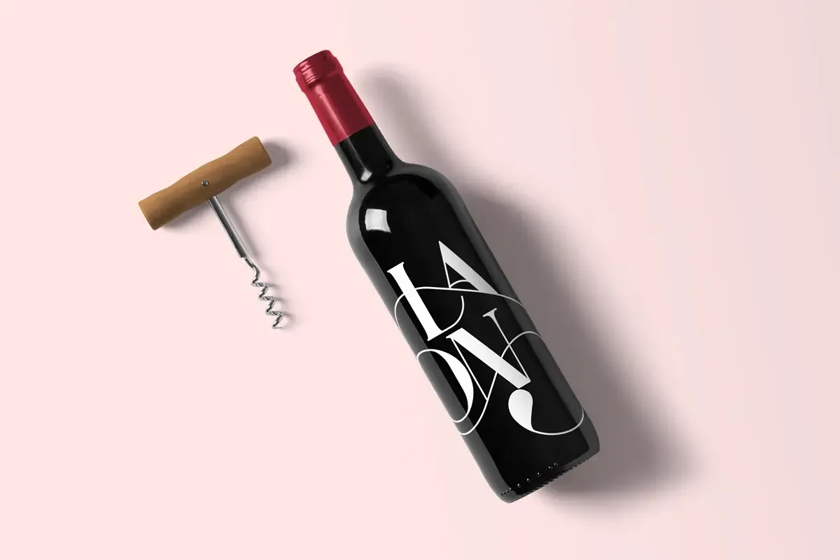 Top-down flat lay of a blank-label wine bottle with foil capsule beside a corkscrew, on a plain light grey background.