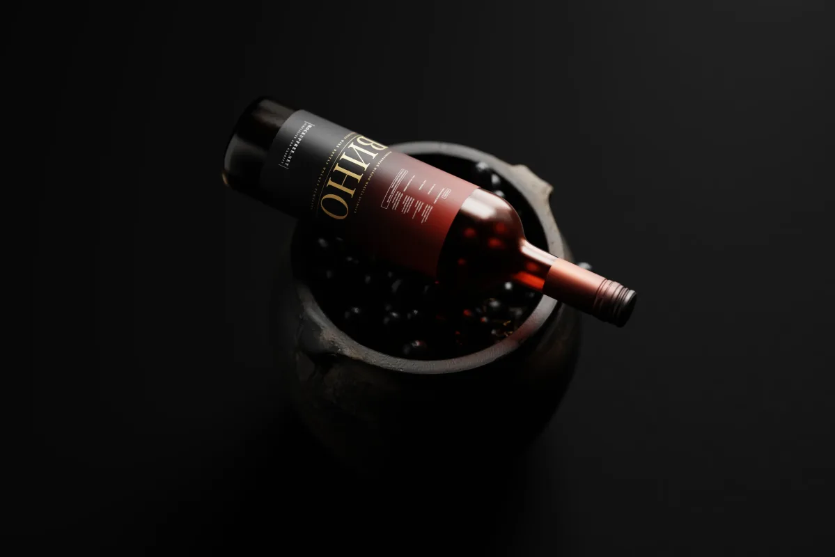 Dark wine bottle mockup with Cyrillic Vino label lying across a wooden barrel filled with grapes, moody low-key lighting.