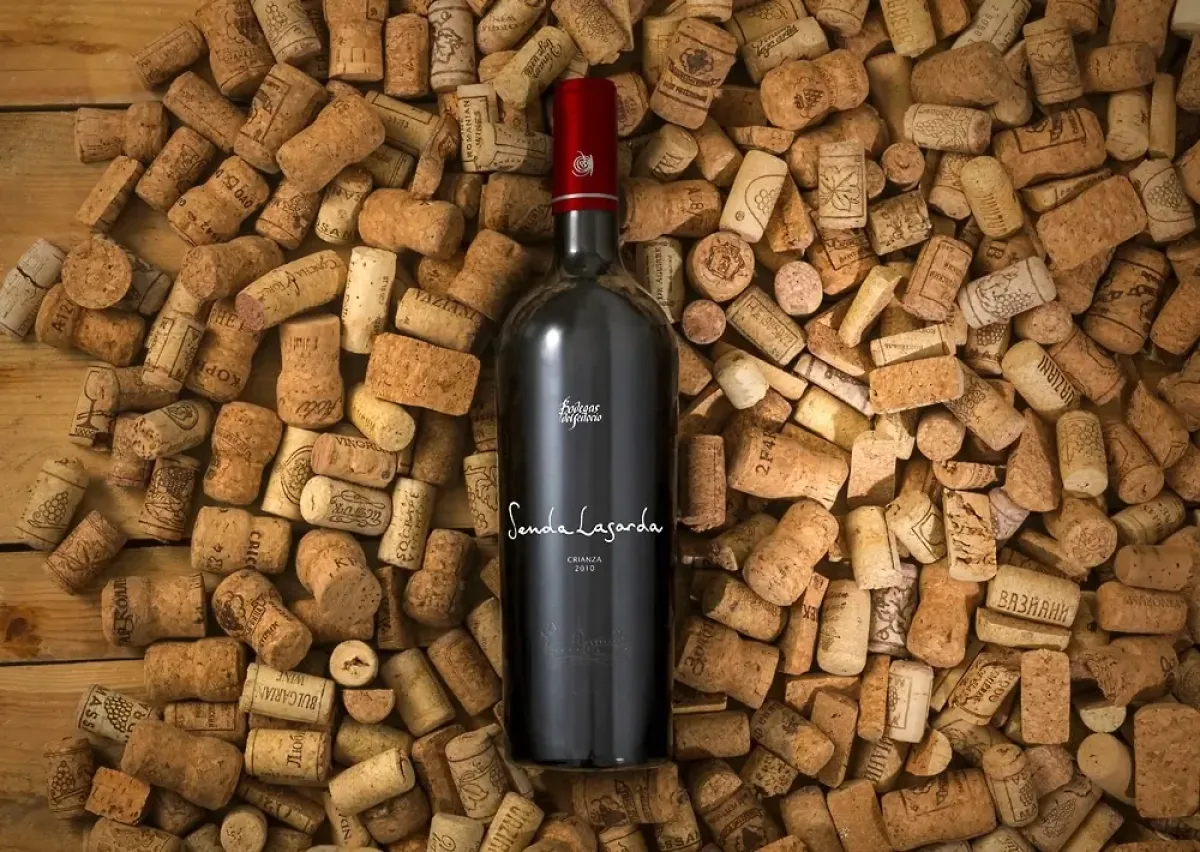 Dark wine bottle with red foil cap and Senda Lasarda label, standing upright surrounded by a dense bed of wine corks on a wooden surface.